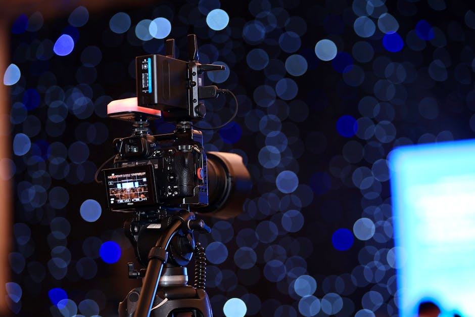 A professional video camera on a tripod with vibrant bokeh lights in the background.